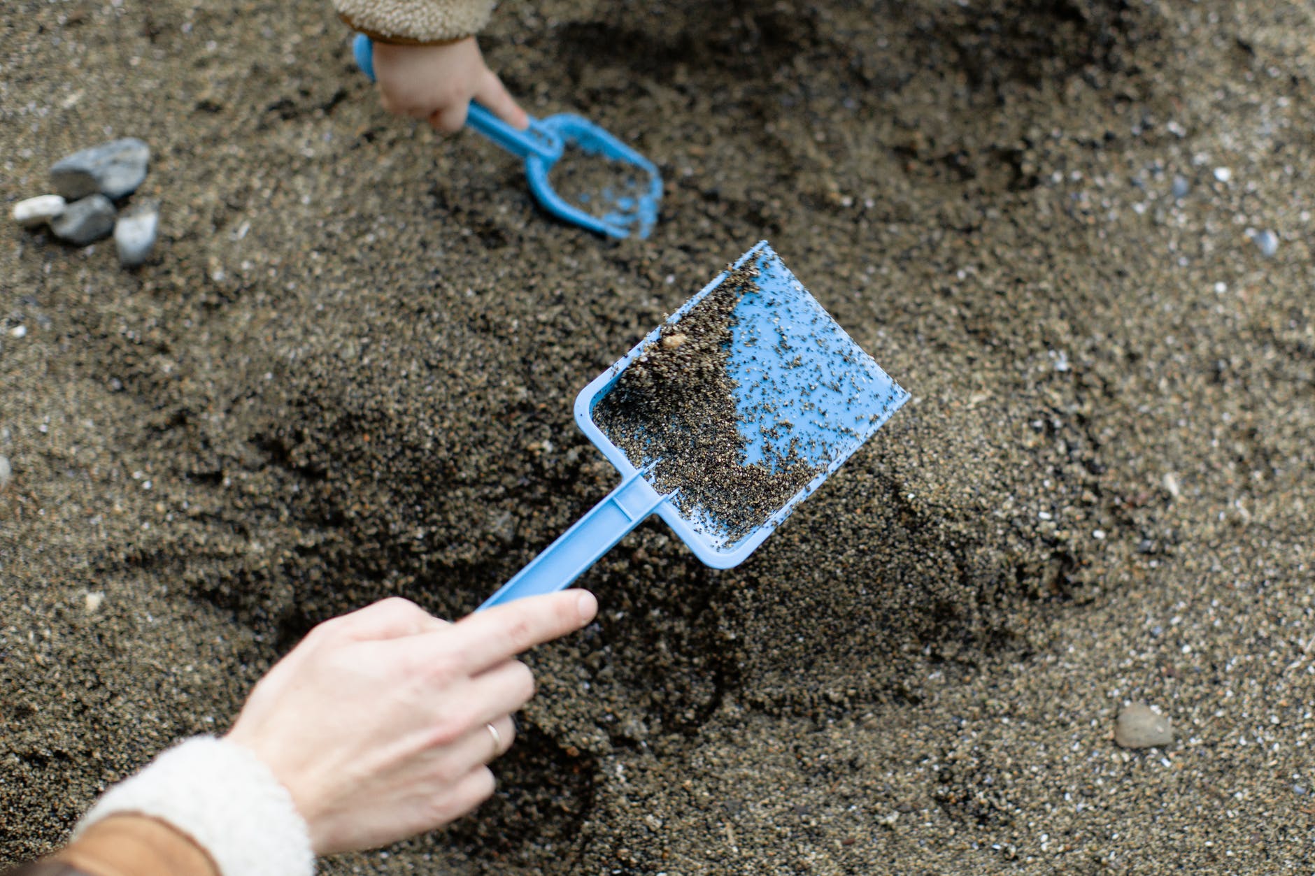 crop faceless mother with baby playing with plastic shovels in sand