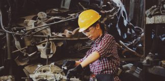 woman wears yellow hard hat holding vehicle part